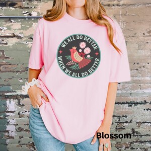 Puede incluir: Camiseta rosa con un gr&aacute;fico de un p&aacute;jaro rojo con flores y el texto "We all do better when we all do better".