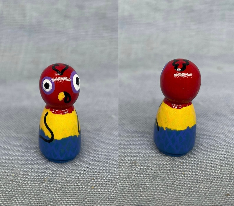 May include: A hand-painted wooden doll with a red head, yellow body, and blue legs. The doll has a black heart shape painted on its head and two large blue eyes.
