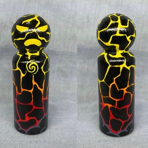 May include: A hand-painted wooden peg doll with a black, yellow, and red lava rock pattern. The doll has a yellow face with black eyes and a black mouth.