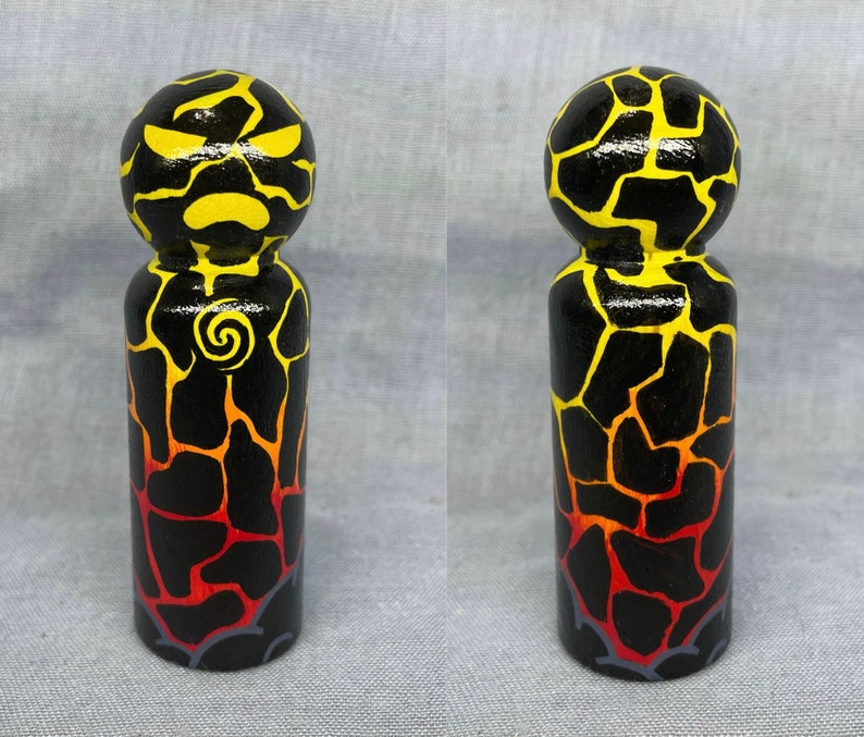 May include: A hand-painted wooden peg doll with a black, yellow, and red lava rock pattern. The doll has a yellow face with black eyes and a black mouth.