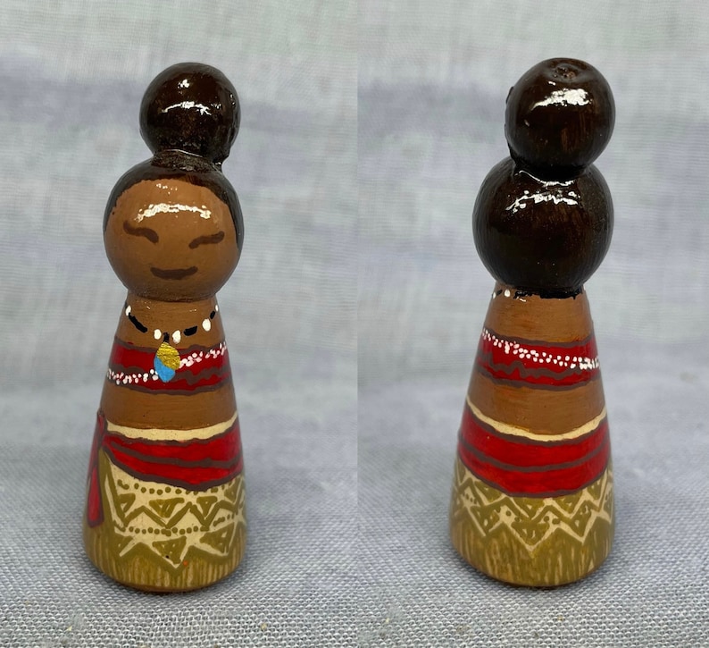 May include: Hand-painted wooden doll with brown hair, a red and brown dress, and a gold and brown skirt. The doll is wearing a necklace with a blue and gold pendant.