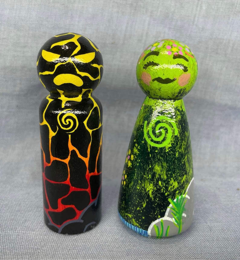 May include: Two hand-painted wooden peg dolls, one with a black and yellow lava-like design and the other with a green and black design with a swirl pattern.
