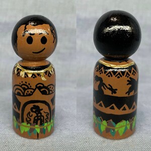 May include: Hand-painted wooden doll with a brown face, black hair, and a black and brown patterned outfit. The doll is wearing a necklace and has a lei around its neck.