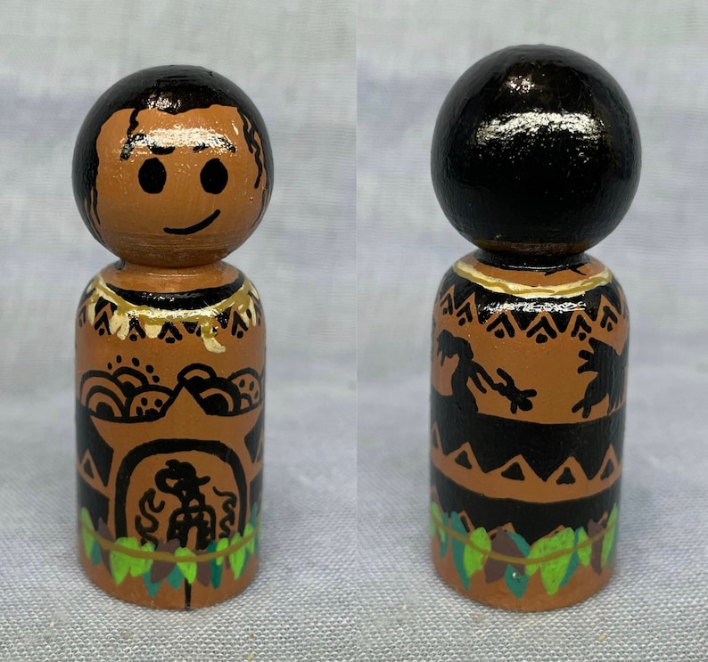 May include: Hand-painted wooden doll with a brown face, black hair, and a black and brown patterned outfit. The doll is wearing a necklace and has a lei around its neck.