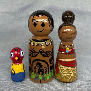 May include: Three wooden peg dolls, one red with a yellow and blue design, one brown with black and white designs and a green lei, and one brown with a red and gold design and a gold necklace.