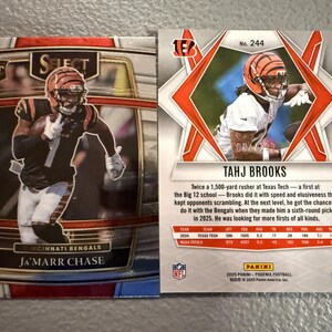 May include: Two football trading cards featuring Cincinnati Bengals players. One card showcases Ja'Marr Chase, the other Tahj Brooks. The cards have action shots of the players in their uniforms, with team logos and player information.