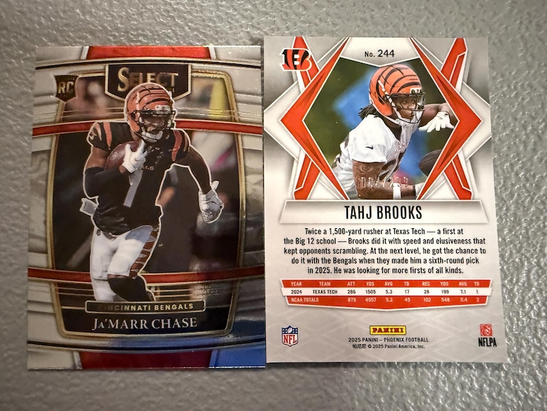 May include: Two football trading cards featuring Cincinnati Bengals players. One card showcases Ja'Marr Chase, the other Tahj Brooks. The cards have action shots of the players in their uniforms, with team logos and player information.