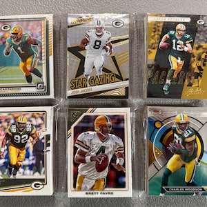 May include: Six collectible football trading cards featuring Green Bay Packers players. The cards are in protective sleeves and showcase players like Aaron Rodgers, Brett Favre, and Charles Woodson. The cards have various designs and include the text "Star Gazing" and "Finest".