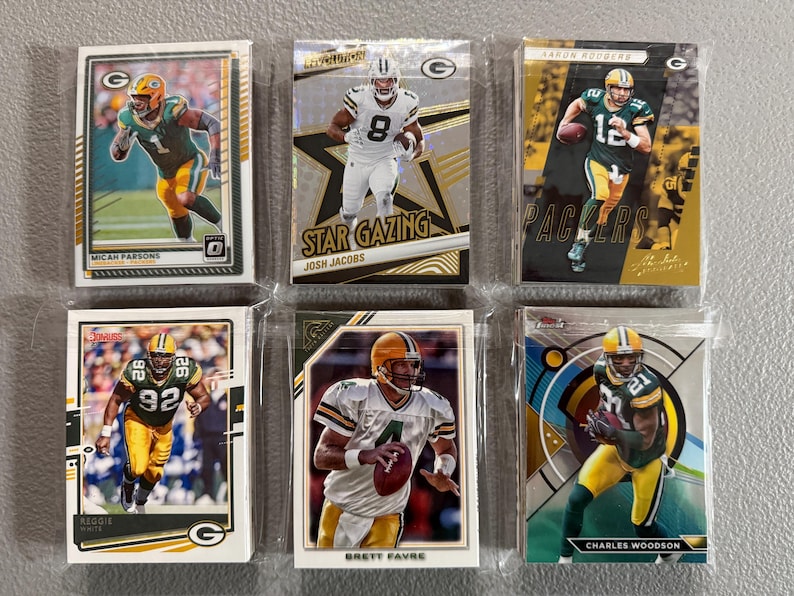 May include: Six collectible football trading cards featuring Green Bay Packers players. The cards are in protective sleeves and showcase players like Aaron Rodgers, Brett Favre, and Charles Woodson. The cards have various designs and include the text "Star Gazing" and "Finest".
