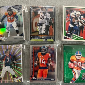May include: Six collectible Denver Broncos football cards in protective sleeves. The cards feature players like Von Miller, Peyton Manning, and Courtland Sutton. The cards have various designs and colors, including orange, blue, and green.