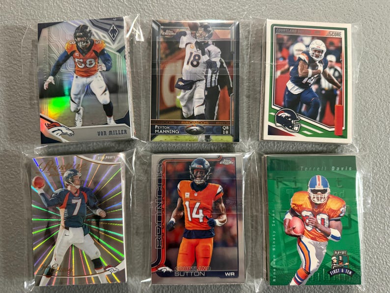 May include: Six collectible Denver Broncos football cards in protective sleeves. The cards feature players like Von Miller, Peyton Manning, and Courtland Sutton. The cards have various designs and colors, including orange, blue, and green.