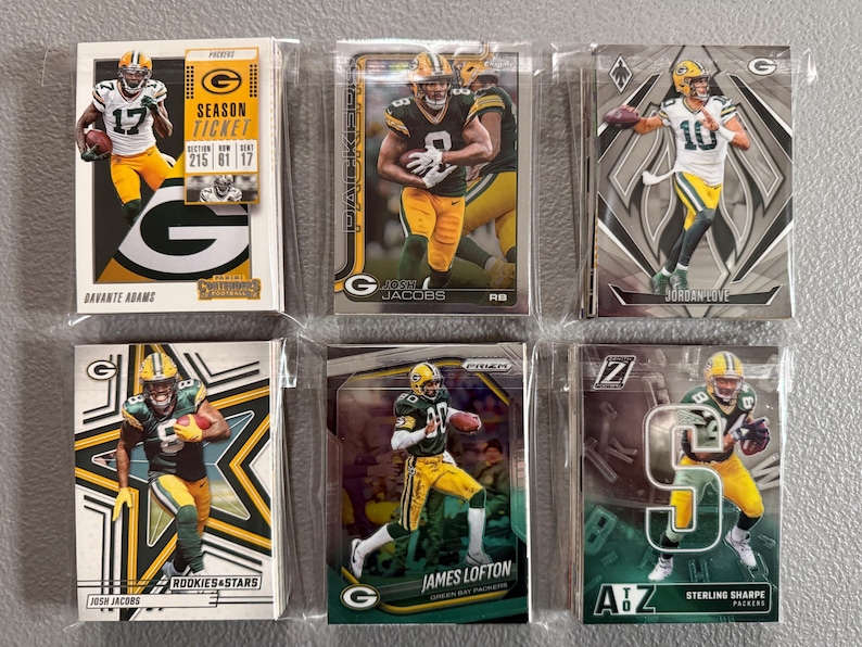 May include: A collection of six football trading cards featuring players in green and yellow uniforms. The cards are in protective sleeves. Players include Davante Adams, Josh Jacobs, James Lofton, and Sterling Sharpe.