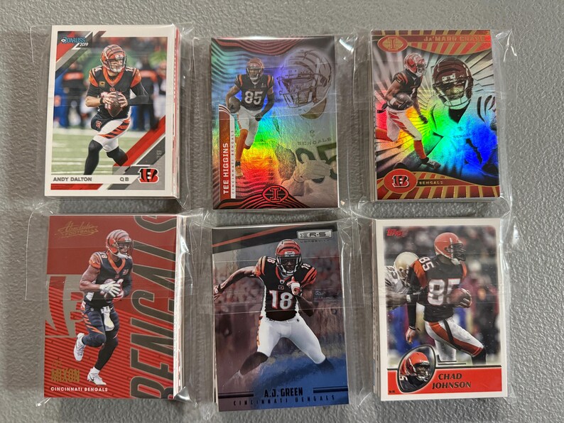 May include: A collection of six Cincinnati Bengals football trading cards, each encased in a protective sleeve. The cards feature images of players like Andy Dalton, Tee Higgins, and Chad Johnson, with team colors of black, orange, and white.