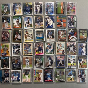 May include: A collection of forty-two Tampa Bay Rays baseball trading cards arranged in a grid. Each card is individually encased in a clear plastic sleeve and features various players in action poses, batting, pitching, or fielding, with team logos.