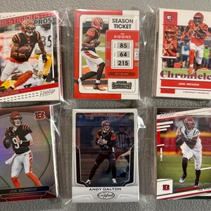 May include: Six trading cards featuring Cincinnati Bengals players, including Joe Burrow, Tee Higgins, and Joe Mixon. The cards are in protective sleeves and display action shots of the players in their uniforms. The cards have the words "Prestige," "Chronicles," and "Certified."