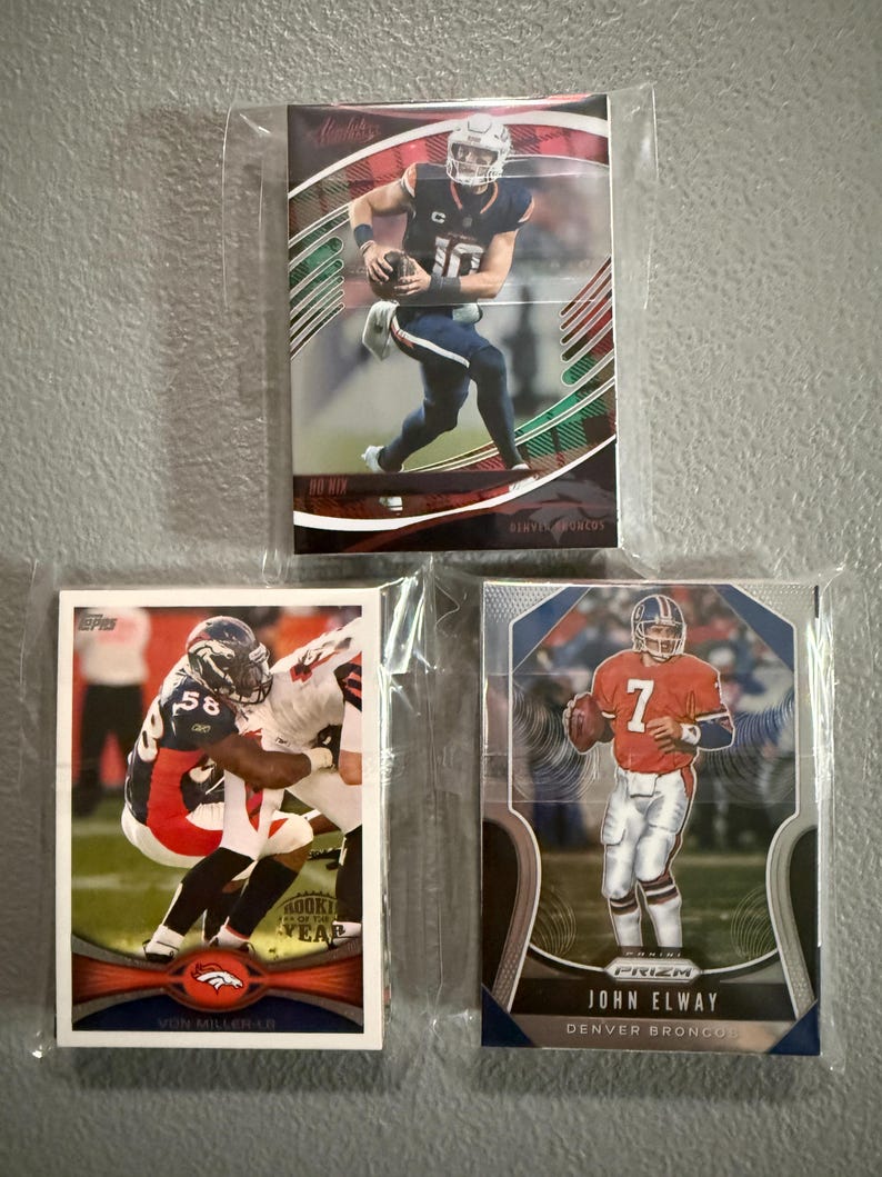 May include: Three Denver Broncos football trading cards in protective sleeves. The cards feature players in action, including a card with the text "John Elway" and another with "Von Miller-LB". The cards are in various designs and colors.