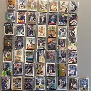 May include: A collection of fifty-two individual Tampa Bay Rays baseball trading cards, each encased in a clear protective plastic sleeve. The cards feature various players in action poses, portraits, and team uniforms, arranged in a grid pattern.