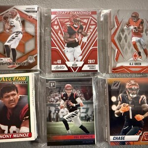 May include: A collection of six Cincinnati Bengals football trading cards. The cards feature players like Joe Burrow, A.J. Green, and Anthony Munoz. The cards are in protective sleeves and have various designs and colors.