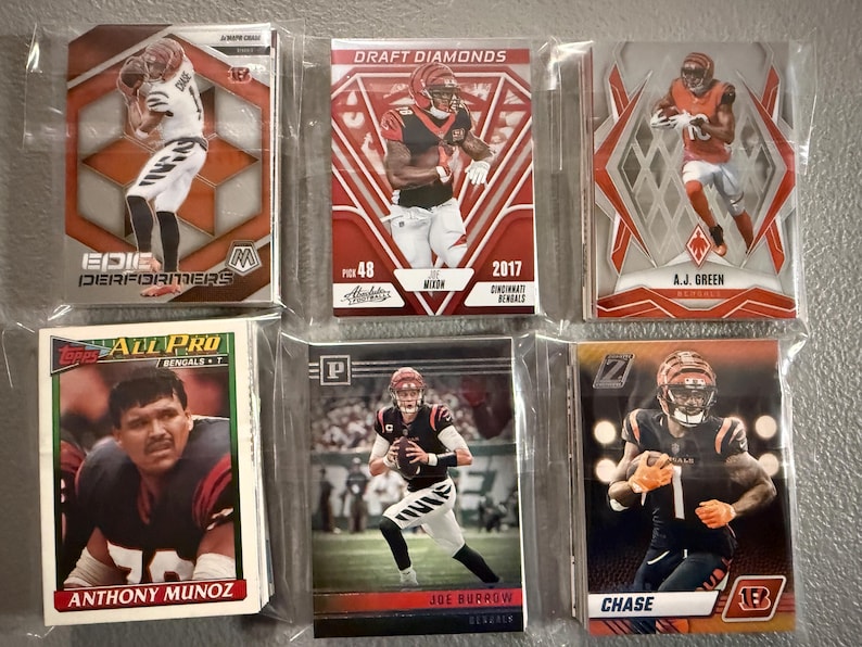 May include: A collection of six Cincinnati Bengals football trading cards. The cards feature players like Joe Burrow, A.J. Green, and Anthony Munoz. The cards are in protective sleeves and have various designs and colors.