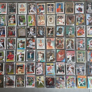 May include: A large collection of rectangular baseball trading cards arranged in a grid. Each card features a color or black and white photograph of a baseball player in various poses, including batting, pitching, and fielding, with some cards displaying team logos.