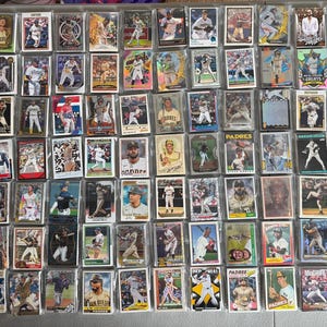 May include: A large collection of rectangular baseball trading cards arranged in a grid. Each card is individually encased in a clear plastic sleeve and features a color photograph of a baseball player in action or a portrait, with various team logos.