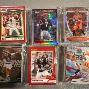 May include: A collection of six football trading cards, each encased in a protective sleeve. The cards feature images of players in action, with team logos and player names visible. The cards are in various designs and colors.