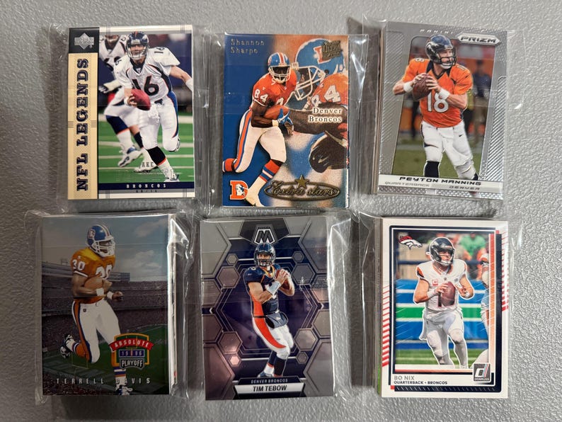 May include: A collection of six Denver Broncos football trading cards in protective sleeves. The cards feature various players, including Peyton Manning and Tim Tebow. The cards are from different sets, with the "NFL Legends" and "Prizm" logos visible.