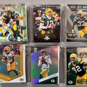 May include: Six Green Bay Packers football trading cards in protective sleeves. The cards feature players like Aaron Rodgers, Davante Adams, and Aaron Jones. The cards have various designs and include the text "Draft Diamonds" and "Quarterback".