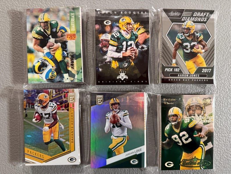 May include: Six Green Bay Packers football trading cards in protective sleeves. The cards feature players like Aaron Rodgers, Davante Adams, and Aaron Jones. The cards have various designs and include the text "Draft Diamonds" and "Quarterback".