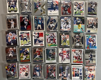 Puede incluir: Una colección de cromos de fútbol, cada uno en una funda protectora, que muestra a jugadores en acción. Las tarjetas presentan a los jugadores con los colores y uniformes del equipo. Algunas tarjetas tienen texto, incluyendo "NOTORIETY" y números de jugadores.