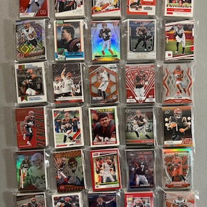 May include: A collection of football trading cards featuring players in orange and black uniforms. The cards are in protective sleeves and showcase various action shots and player portraits. Some cards have text like "Chad Johnson" and "Cincinnati".