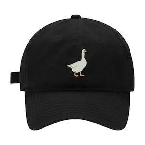Puede incluir: Una gorra de béisbol negra con un gráfico bordado de un ganso blanco con pico y patas naranjas centrado en el panel frontal. La gorra tiene una visera curva, un botón en la parte superior y una correa ajustable en el lateral.