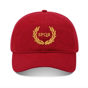 May include: A red baseball cap with a gold embroidered laurel wreath and the text "SPQR" in the center.