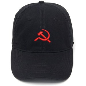 Puede incluir: Una gorra de béisbol negra con un símbolo de martillo y hoz bordado en rojo.
