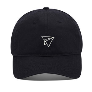 Peut inclure: Casquette de baseball noire avec un motif d'avion en papier blanc brodé. La casquette a une visière incurvée et une sangle réglable à l'arrière. Un accessoire simple et élégant.