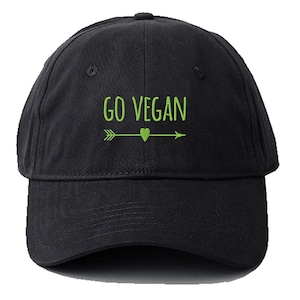 Può includere: Un berretto da baseball nero con un designo di freccia e cuore ricamato in verde. Il testo "GO VEGAN" è ricamato in verde sulla parte anteriore del berretto.