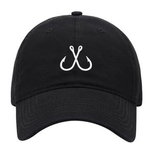 May include: A black baseball cap featuring an embroidered white graphic of two crossed fishing hooks centered on the front panel. The cap has a curved brim, a button on the top, and stitched eyelets for ventilation on the crown.