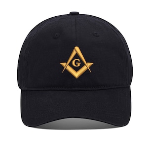 Puede incluir: Una gorra de béisbol negra con un símbolo masónico bordado en oro, que incluye una brújula y una escuadra con una 'G' en el centro.