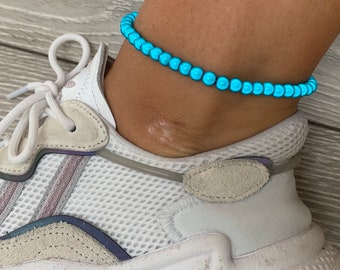 May include: A turquoise blue beaded anklet on a person's ankle. The anklet is made of small, round beads that are strung together on a thin cord.