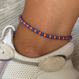 May include: A blue and orange beaded ankle bracelet. The bracelet is made of small, round beads that are strung together on a thin cord.