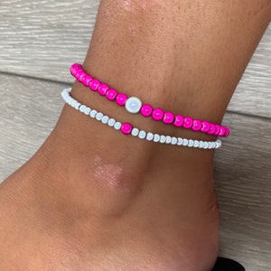 Könnte beinhalten: Zwei Perlenarmbänder, eines weiß und eines pink, mit einem weißen Perlenanhänger am pinken Armband.