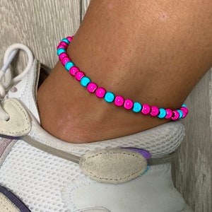 May include: A pink and blue beaded anklet. The anklet is made of small, round beads that are alternating colors.