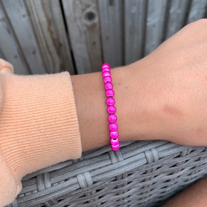 May include: A pink beaded bracelet with a shiny finish. The bracelet is made of small, round beads that are strung together on a thin cord.