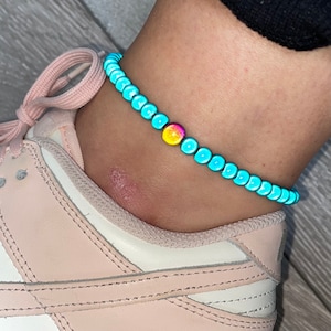 May include: A turquoise blue beaded anklet with a single yellow and pink bead in the centre.