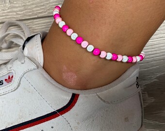 May include: A pink, white, and light pink beaded anklet. The anklet is made of small, round beads.