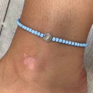 May include: A light blue beaded anklet with a silver seashell charm.