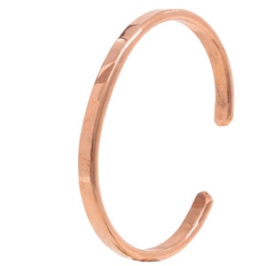 Könnte beinhalten: Ein kupferfarbenes Armreif-Armband. Das offene Armband hat ein schlichtes, minimalistisches Design. Das Metall hat eine polierte Oberfläche, die das Licht reflektiert. Das Armband ist ein einzelnes, durchgehendes Band, ca. 6,35 cm im Durchmesser.