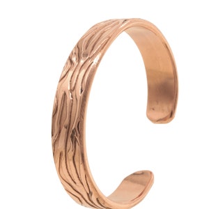 Könnte beinhalten: Ein Zehenring aus Kupfer mit einem strukturierten Holzmaserungsmuster.