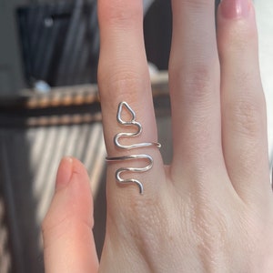 May include: A silver snake-shaped ring worn on a finger.