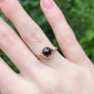 Op de afbeelding: Een ring van goudkleurig draad met een donkerrode edelsteen.